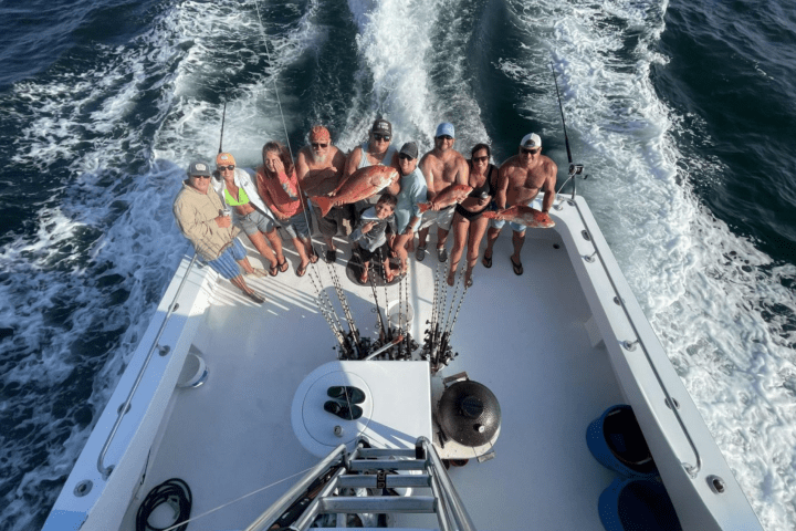 Group of people on a boat holding fish, with ocean waves in the background.