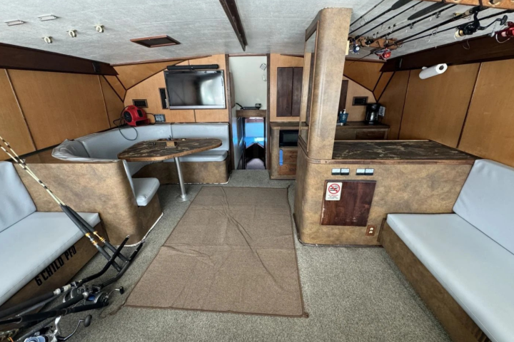 Interior of a boat with a seating area, TV, fishing rods, and storage compartments.