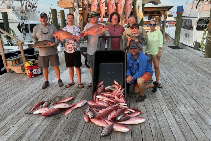 Group of people on a dock with a large collection of fish, some displayed on a rack behind them.