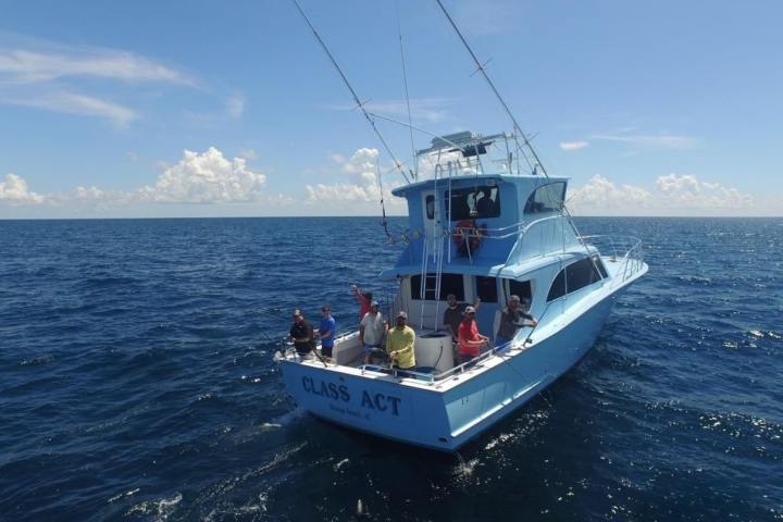 A group of people on a boat named 'Class Act' in the ocean under a clear blue sky.