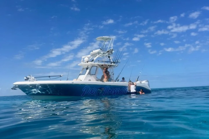 A boat named 'Pier Pressure' on clear blue water under a partly cloudy sky.