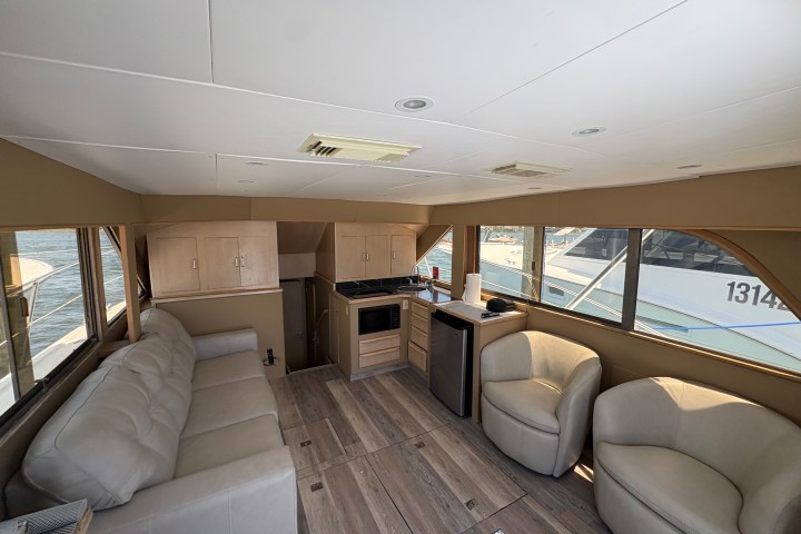 Interior of a yacht with sofa, chairs, kitchenette, and large windows.