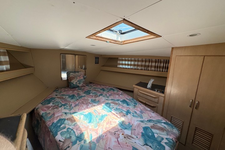 Cozy boat cabin with bed, skylight, wooden cabinets, and striped curtains.