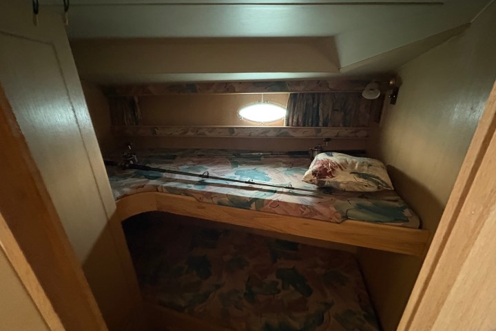 Dimly lit bunk beds with fishing rods and pillows in a compact space.