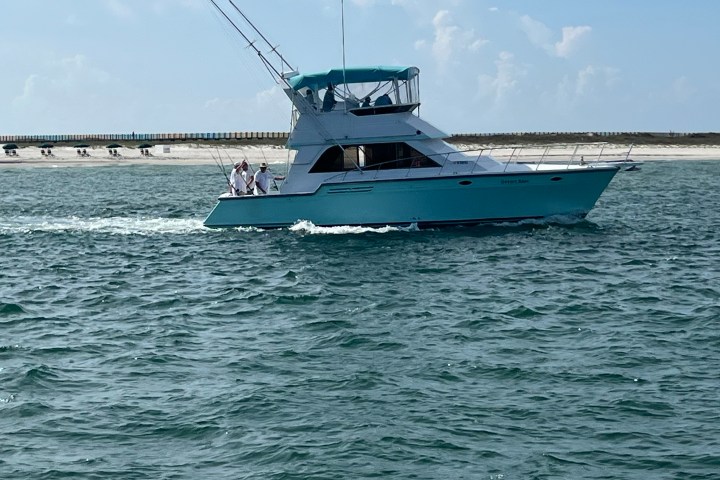 Blue yacht cruising near a sandy shoreline with a clear sky.
