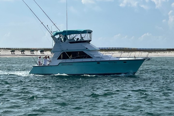 Turquoise fishing boat on water with beach in background.