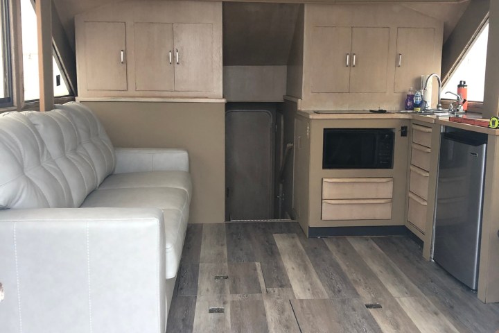 Modern trailer interior with sofa, cabinets, microwave, and mini-fridge.