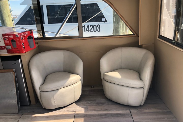 Two beige chairs in a boat cabin with windows showing a docked boat.
